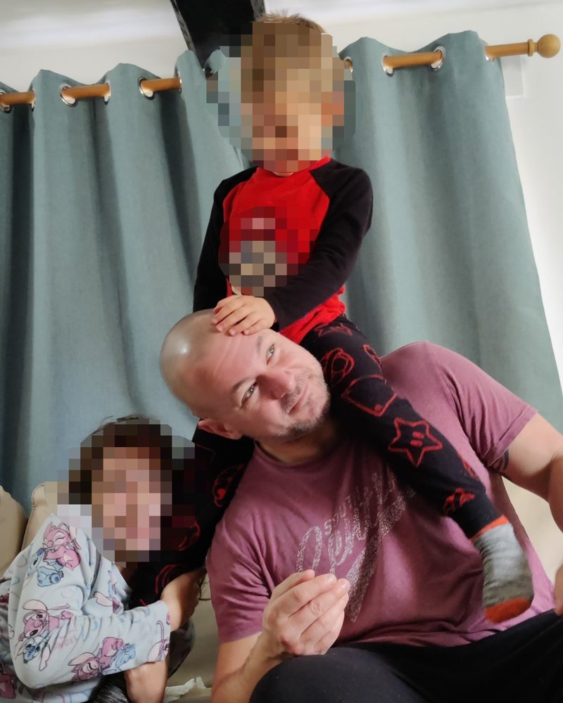 Ricky at home on the sofa, one of his children on his shoulders and another beside him